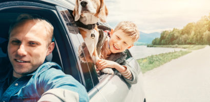 Father, son, and dog hanging out of the window of a moving car