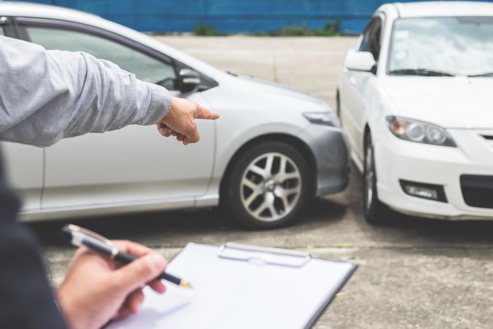 one hand points to car accident while another hands fills out an insurance form