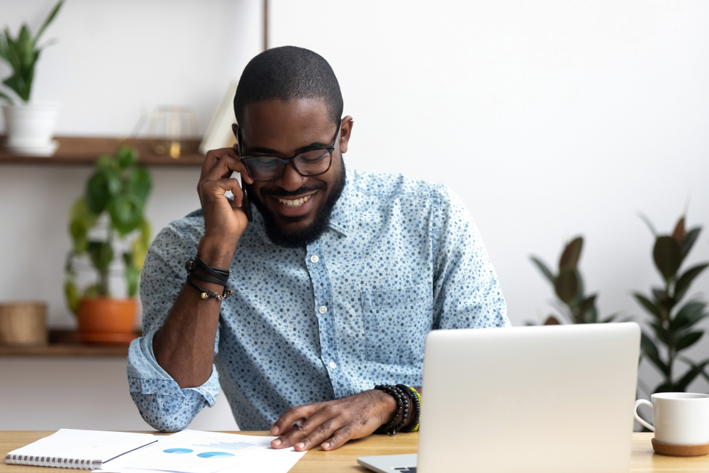 man talks on phone while sitting at desk in home office