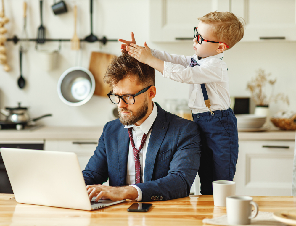 businessman works at computer while small child plays with his hair