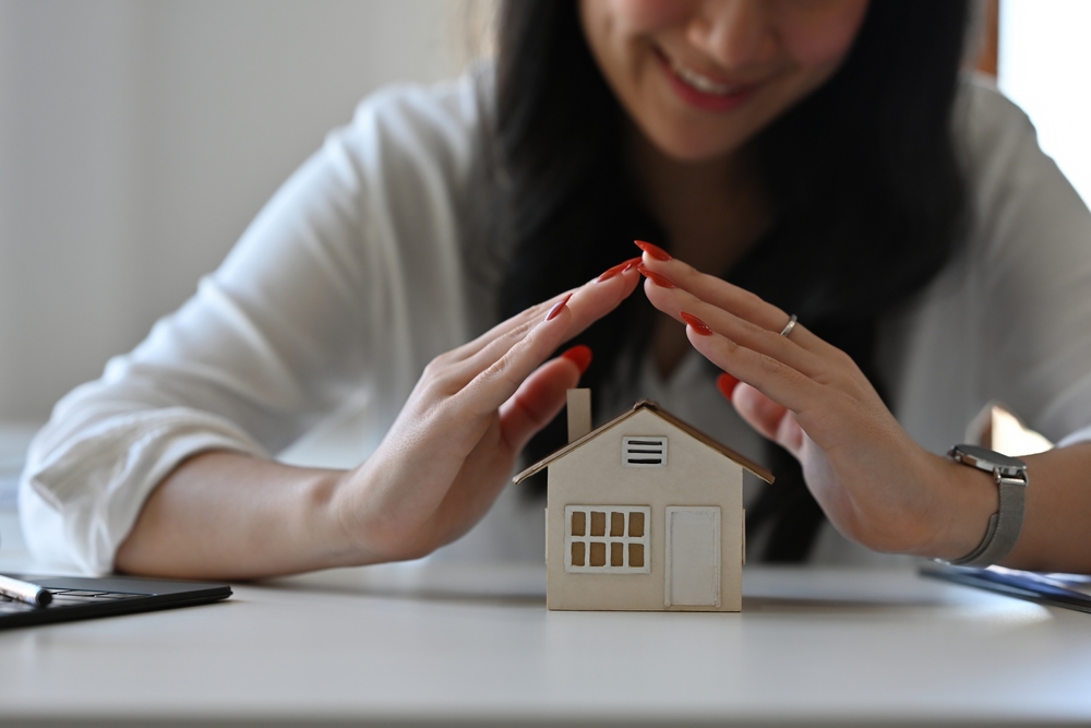 hands protect house model to symbolize insurance coverage