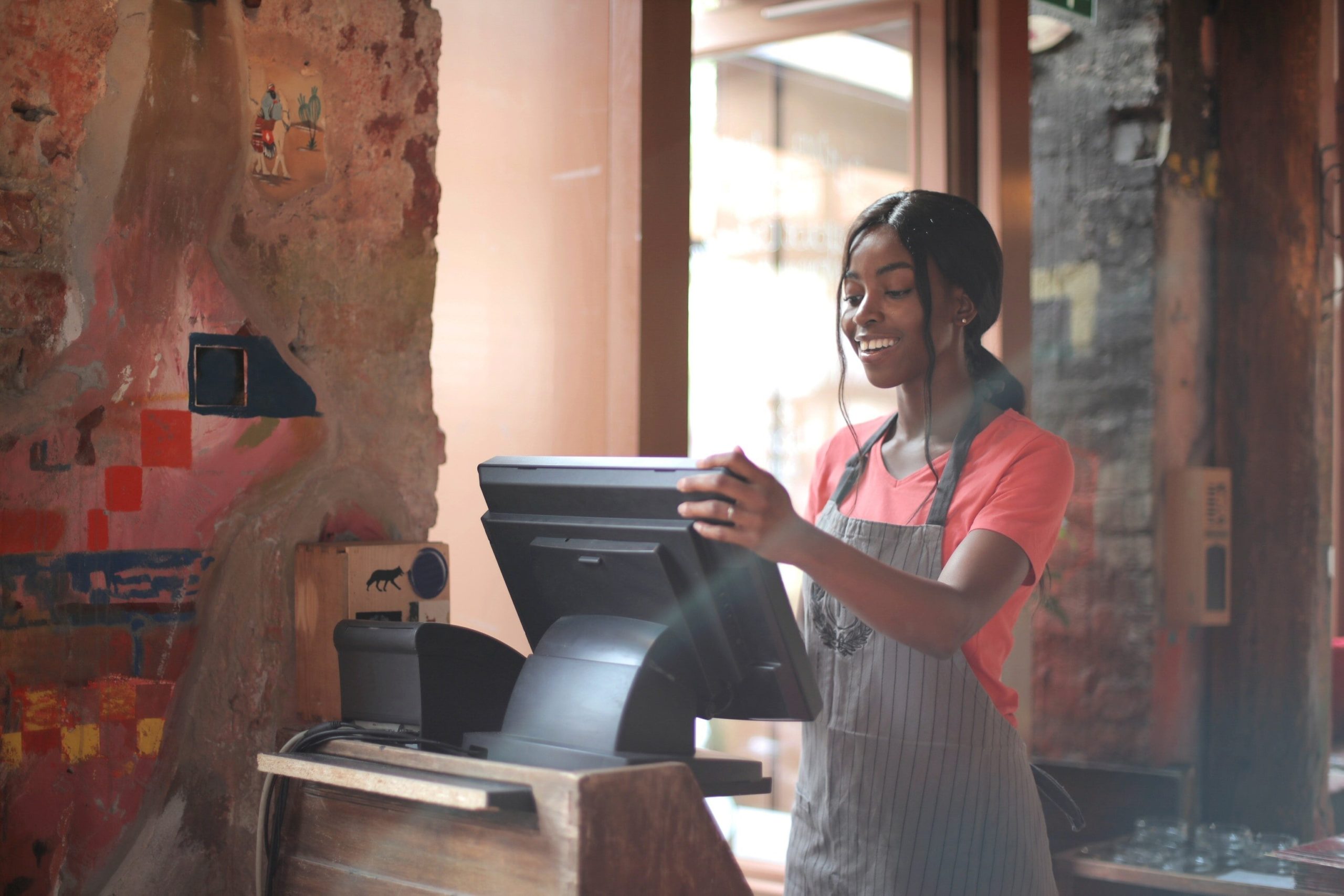 Cashier wearing grey apron stands at checkout and POS system