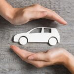 two hands hold cutout of car above wooden desk
