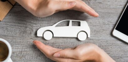 two hands hold cutout of car above wooden desk