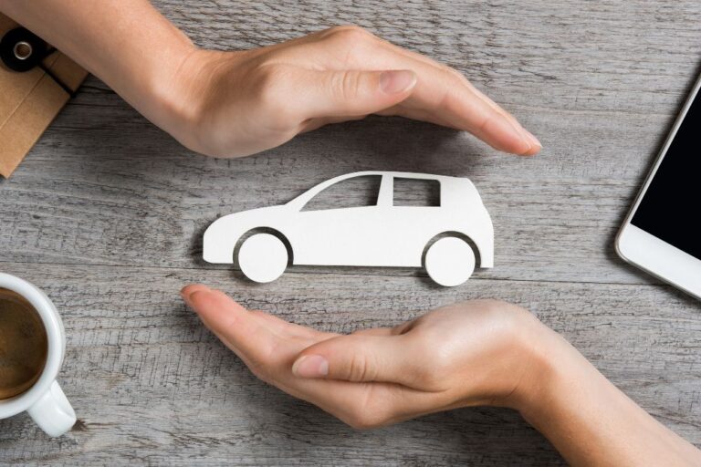 two hands hold cutout of car above wooden desk
