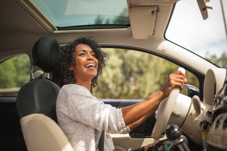Woman smiling while driving a car on a sunny day