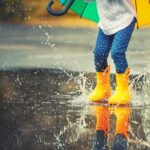 Child wearing rain boots and holding an umbrella while jumping in puddles