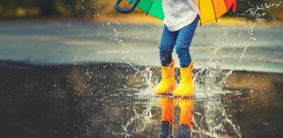 Child wearing rain boots and holding an umbrella while jumping in puddles