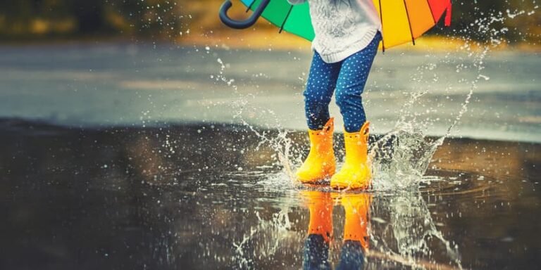Child wearing rain boots and holding an umbrella while jumping in puddles