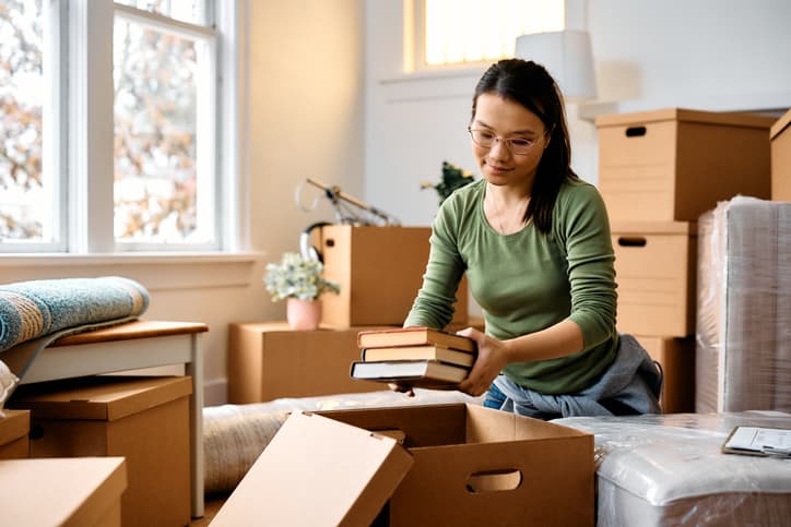 Woman packing books into moving boxes inside a new home