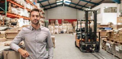 Man standing in a warehouse with inventory shelves and a forklift in the background