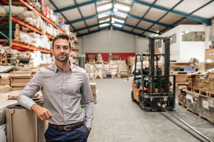 Man standing in a warehouse with inventory shelves and a forklift in the background