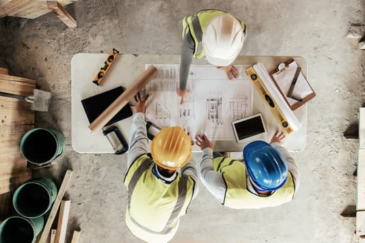 Construction team reviews building plans and measurements at a job site table