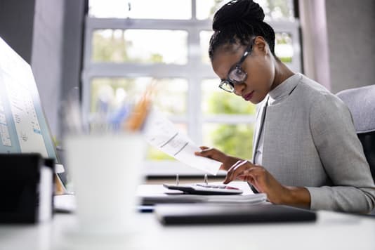 Office professional reviews a document while calculating numbers at a desk